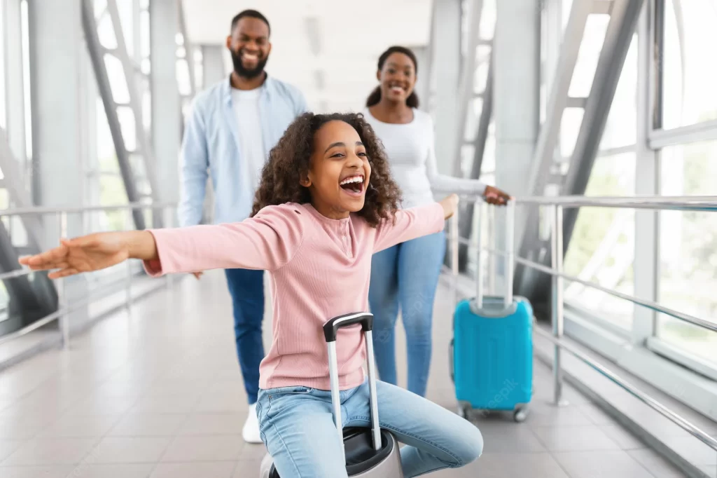 happy loving family airport portrait joyful excited black girl sitting suitcase laughing spreading arms imitating plane smiling cheerful parents walking blurred background 568137 823
